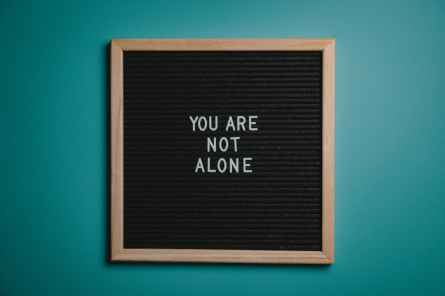 you are not alone quote board on brown wooden frame